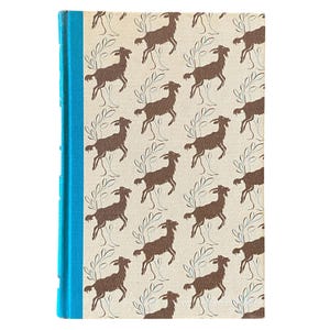 May include: A hardcover book with a light beige cover featuring a repeating pattern of brown goats and stylized green branches. The spine is a bright turquoise blue.
