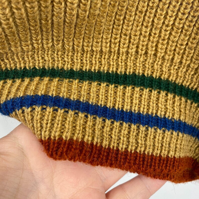 May include: Close-up of a knitted fabric with a mustard yellow base and stripes of dark green, blue, and rust.