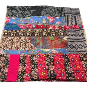 Puede incluir: Una funda de cojín patchwork con una variedad de telas estampadas en negro, azul, rojo y rosa. Las telas presentan diseños florales, geométricos y abstractos. La funda del cojín tiene un borde de color neutro.