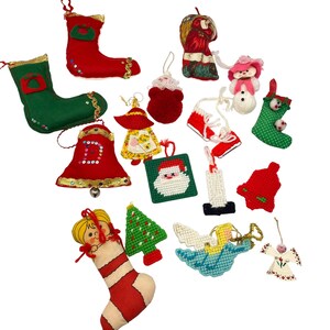 Könnte beinhalten: Eine Sammlung von Vintage-Weihnachtsschmuck in verschiedenen Formen und Farben. Enthält rote und grüne Strümpfe, Glocken, ein Santa Claus-Quadrat, einen Schneemann, eine Kerze, einen Engel und einen Weihnachtsbaum. Ornamente sind aus Stoff und Garn.