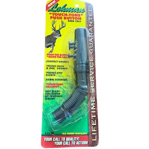 Puede incluir: Un llamador de ciervos negro con un tubo flexible y acanalado y un botón. El embalaje es verde y amarillo, con el texto "TOUCH-TONE PUSH BUTTON DEER CALL". Incluye una garantía de servicio de por vida.