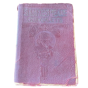 May include: A vintage, burgundy-colored book titled "Shakespeare Complete." The cover features embossed text and a portrait of William Shakespeare within a circular frame. The book's edges show signs of wear, suggesting its age.