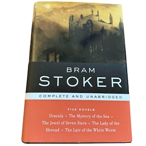 May include: A hardcover book featuring the author Bram Stoker. The book cover has a dark, gothic illustration of a castle and a sunset. The title "Bram Stoker" is in white letters on a black band. The book includes five novels.