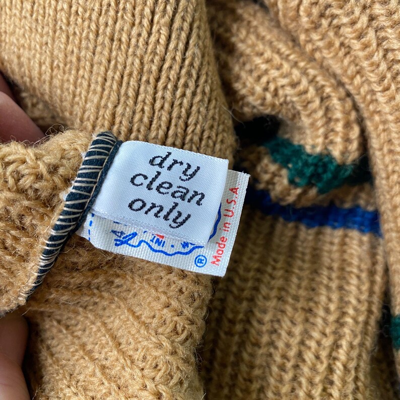 May include: Close-up of a brown knit sweater with a green and blue striped pattern. The sweater has a white care label that reads "dry clean only" and "Made in U.S.A."
