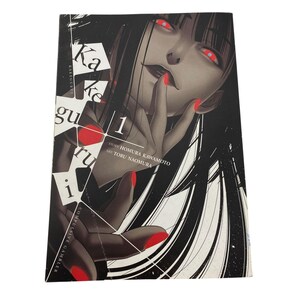 May include: Kakegurui Compulsive Gambler Volume 1 manga book. The cover features a woman with long black hair, red eyes, and red nail polish. The title and author's names are printed on the cover.