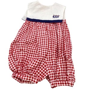 May include: A vintage baby romper with a red and white gingham pattern. The romper features a white collar with a navy blue trim and embroidered figures. The garment has a loose, comfortable fit, perfect for warm weather.
