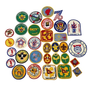 May include: A collection of vintage embroidered patches in various shapes and sizes. The patches feature text and graphics related to scouting, sports, and patriotic themes. Colors include green, yellow, red, and blue. Some patches have text like "Patrol Leader" and "YMCA Basketball".