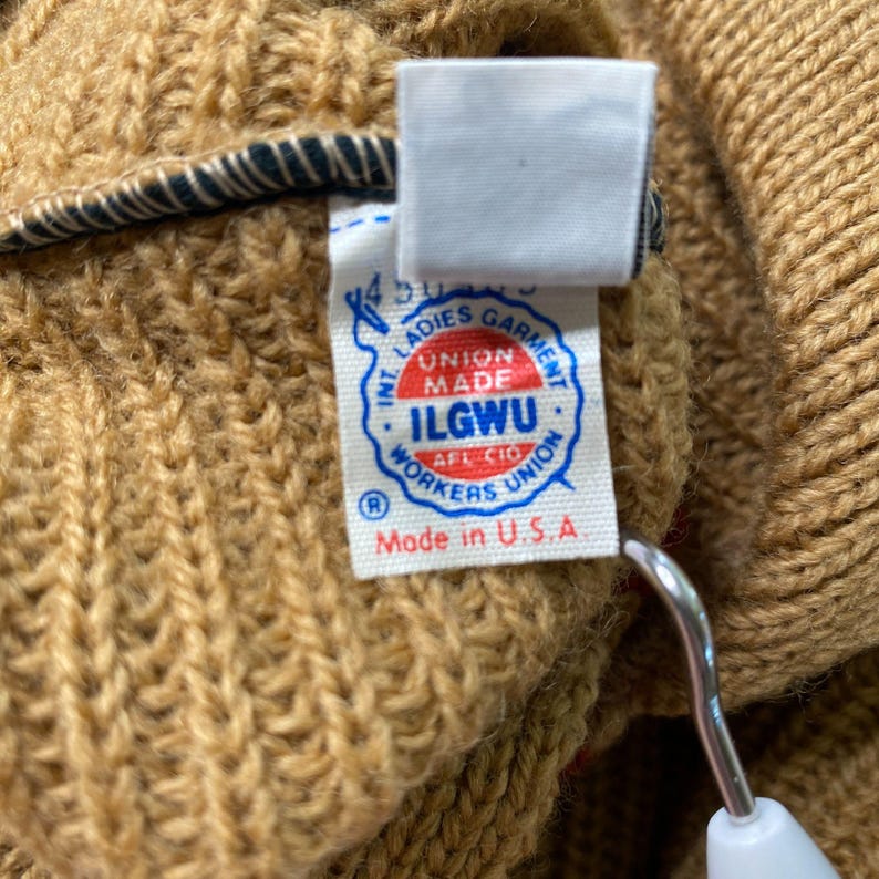 May include: A brown knitted sweater with a white label that reads "Int. Ladies Garment Workers Union Made ILGWU AFL-CIO Workers Union R Made in U.S.A."