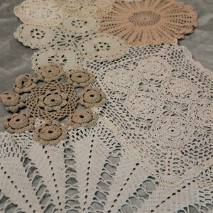 May include: A collection of white and cream crocheted doilies of various sizes and patterns arranged on a gray surface.