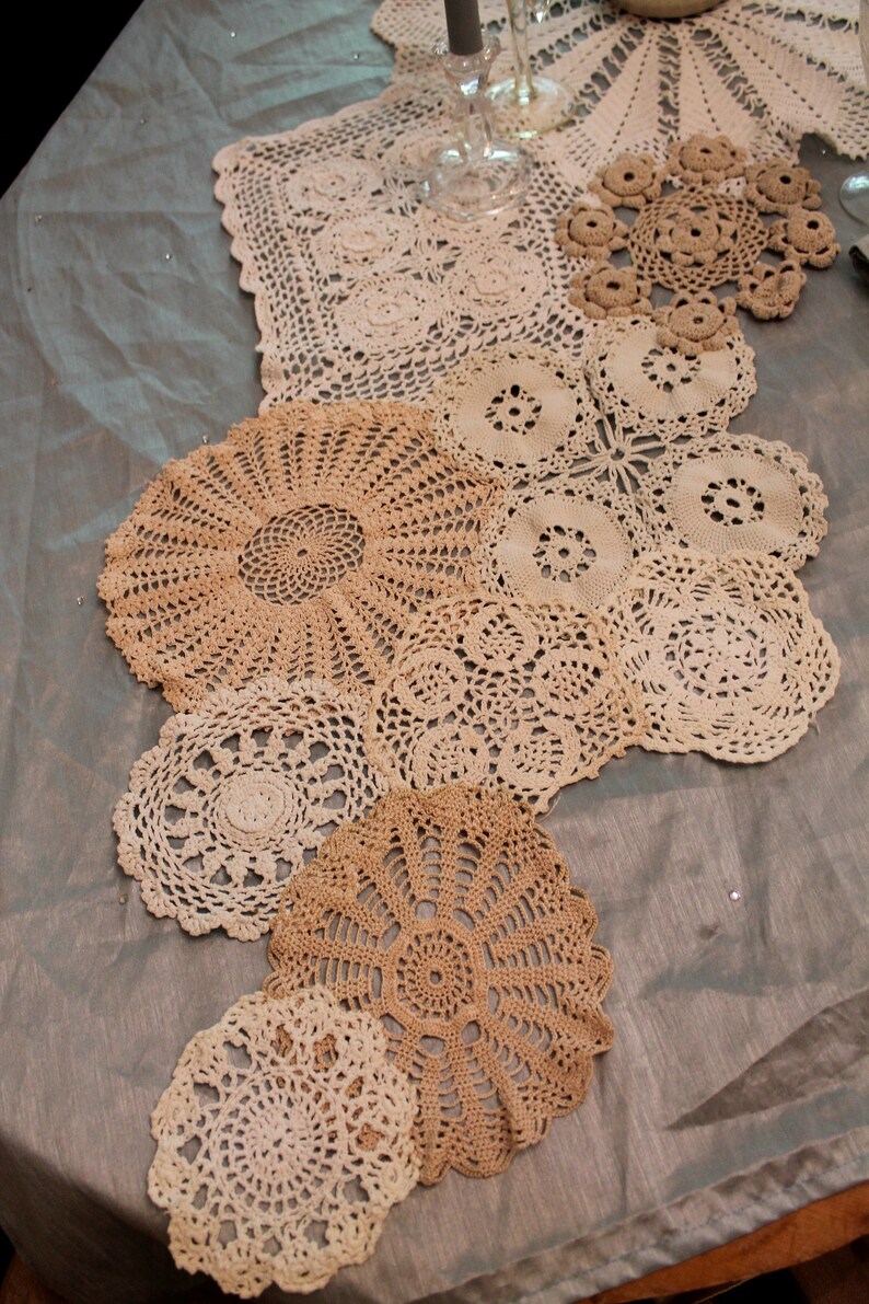 May include: A collection of crocheted doilies in various sizes and patterns, arranged in a cascading design on a light gray tablecloth.