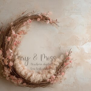 May include: A circular newborn photography prop featuring a woven twig wreath adorned with pink flowers. The center is filled with soft, light-colored fluff. The background is a textured, neutral-toned surface. Text on the image reads "May & Moss" and "Newborn digitals by lori lesh photography."