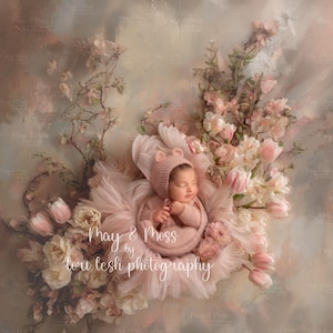 May include: A newborn baby swaddled in a pink outfit with a matching bear-eared hood, nestled in a bed of pink tulle and flowers. The background is a soft, pastel-colored backdrop. The image is signed "May & Moss by tori lesh photography."