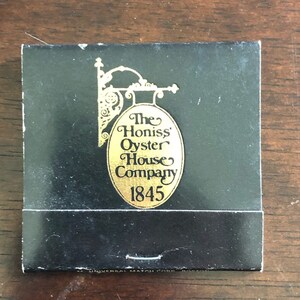 May include: A black matchbook with a gold oval logo that reads "The Honiss' Oyster House Company 1845".