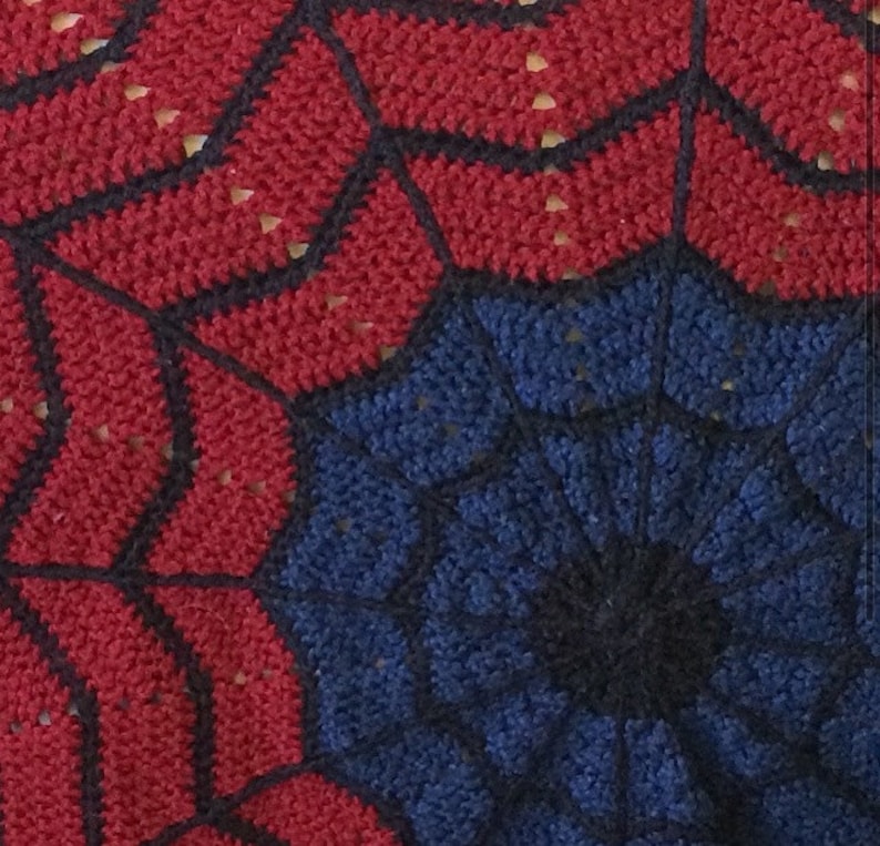 May include: A close-up of a crocheted spider web design in red and blue yarn. The center of the web is black.