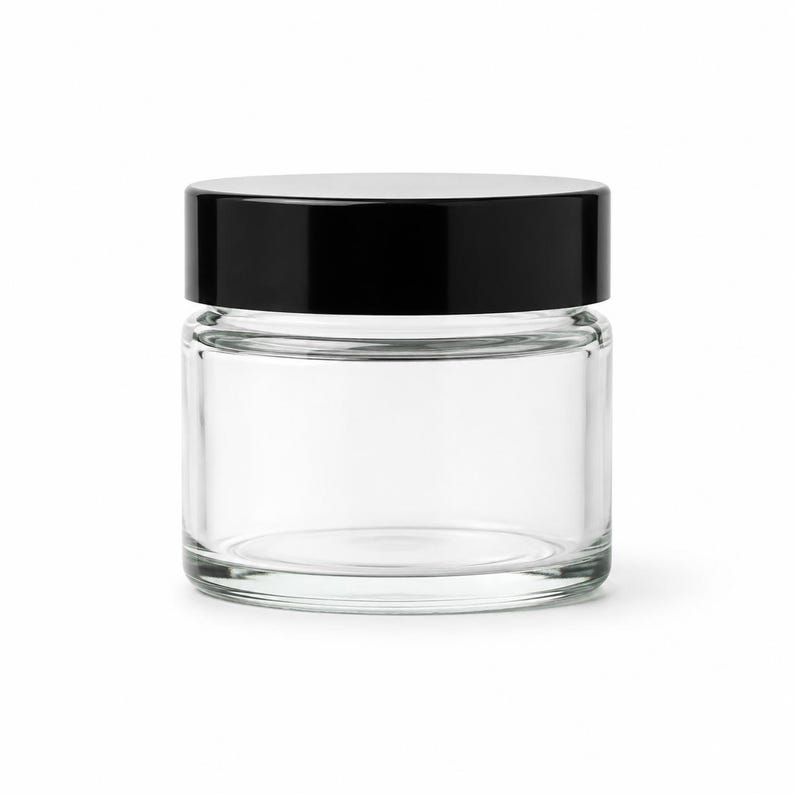May include: A clear, cylindrical glass jar with a smooth, flat base and a thick, glossy black screw-top lid. The container features a wide opening and transparent walls, showcasing a simple, functional design for storage or cosmetic use.