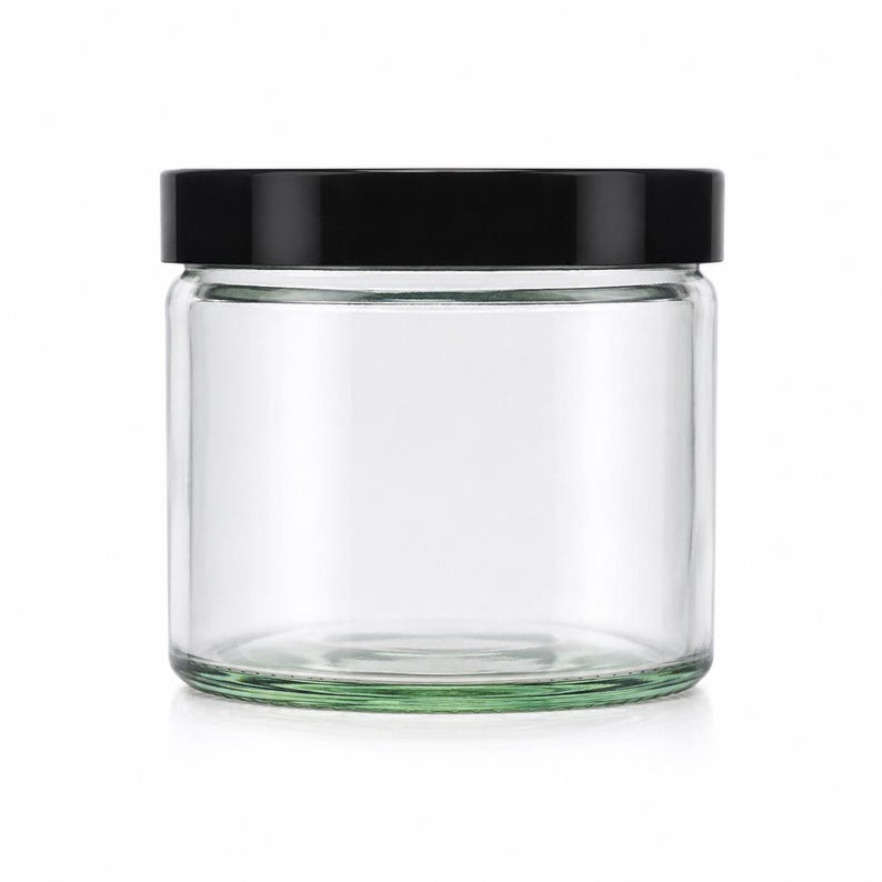 May include: A clear, cylindrical glass jar with a smooth, transparent body and a flat, solid black screw-top lid. The container features a wide mouth and a sturdy, thick base, providing a simple and functional design for storage and organization.