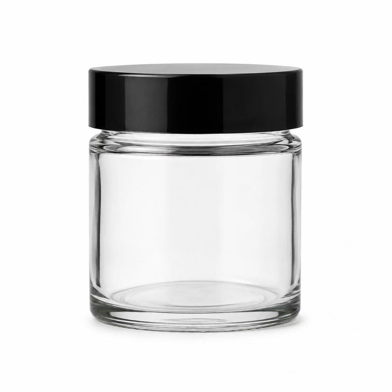 May include: A clear glass jar with a smooth, cylindrical body and a flat, solid black screw-top lid. The container features a wide mouth and a thick, sturdy base, providing a transparent view into the interior space of the empty storage vessel.