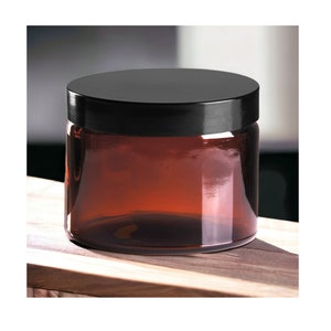 May include: A brown glass jar with a black lid. The jar is empty and sitting on a wooden surface.