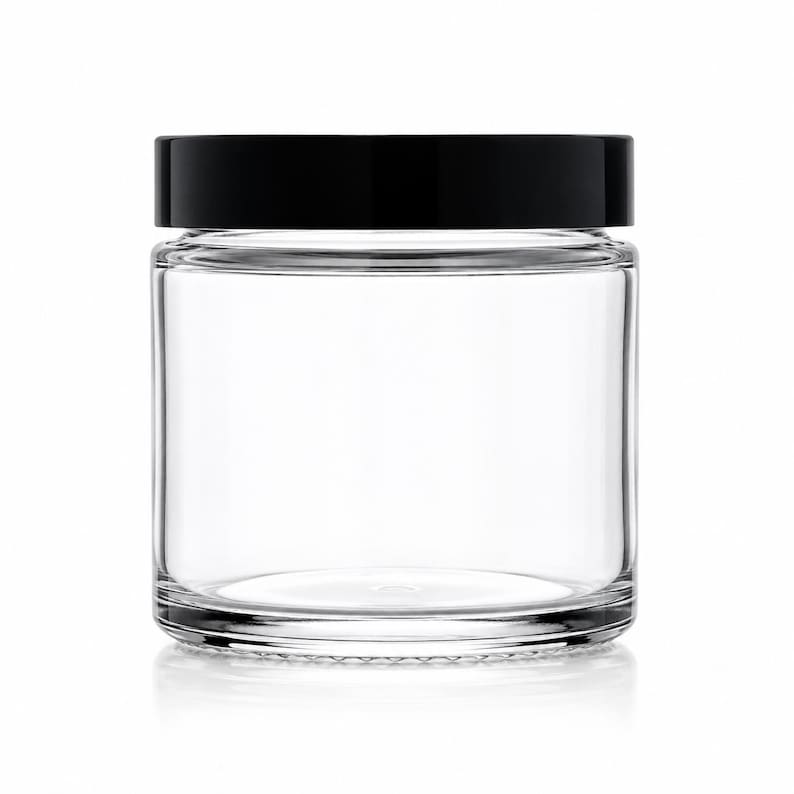 May include: A clear, cylindrical glass jar with a smooth, transparent body and a flat, solid black screw-top lid. The container features a wide mouth and a thick, sturdy base, providing a simple and functional design for storage or display purposes.