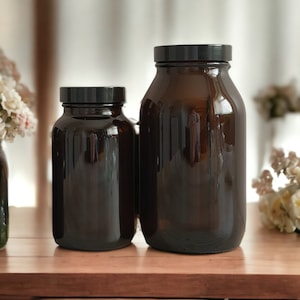 May include: Two amber glass bottles with black lids. The larger bottle is taller and wider than the smaller bottle. Both bottles are empty and have a smooth, shiny surface.