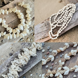 May include: A collection of seashell necklaces displayed on weathered wood and sand. The necklaces feature various shell types, showcasing natural colors and textures. Some are strung together, while others are arranged in a circular pattern.
