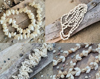 May include: A collection of seashell necklaces displayed on weathered wood and sand. The necklaces feature various shell types, showcasing natural colors and textures. Some are strung together, while others are arranged in a circular pattern.
