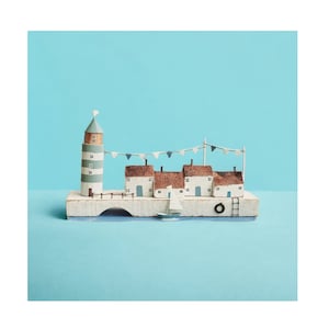 Pu&ograve; includere: Un villaggio costiero in miniatura di legno con un faro, case, un ponte e una barca a vela. Le case hanno pareti bianche, tetti marroni e dettagli blu. Il faro &egrave; a strisce blu e bianche. Il ponte &egrave; bianco con un arco blu. La barca a vela &egrave; bianca con una vela blu. Il villaggio &egrave; posto su una base di legno.