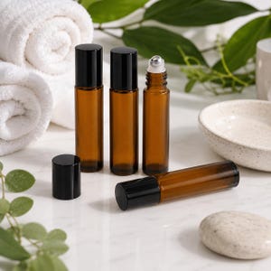 May include: Four amber glass roller bottles with black caps. Three bottles stand upright, one with the cap removed to reveal a silver metal roller ball, while the fourth bottle lies horizontally on a white surface next to a black cap.