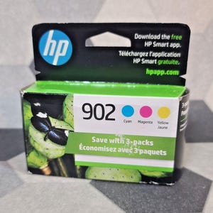 Op de afbeelding: Een HP 902 inktcartridge doos met een groen en zwart ontwerp. De doos heeft het HP-logo, de woorden "Cyaan, Magenta, Geel" en de tekst "Save with 3-packs". De doos bevat ook een vlindergrafiek.