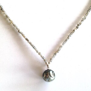 Puede incluir: Un collar de plata con un colgante redondo gris con un dise&ntilde;o de espiral. El collar est&aacute; hecho de peque&ntilde;as cuentas facetadas.