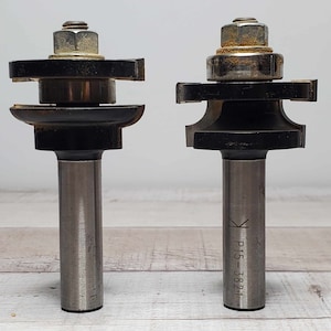 May include: Two router bits with black and silver metal bodies and a silver shaft. The bit on the right has the text "P15-3821" engraved on the shaft.