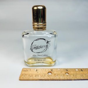 Pu&ograve; includere: Flacone di dopobarba Stetson in vetro trasparente con tappo dorato. Il flacone ha una forma rettangolare con bordi arrotondati e un logo nero. Contiene 59 ml di dopobarba. Un righello di legno &egrave; in primo piano.