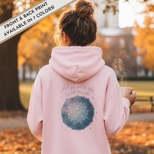 May include: A light pink hoodie with the text "Align with the Universe" and a blue and white mandala design on the back. The hoodie also has the text "FRONT & BACK PRINT AVAILABLE IN 7 COLORS!" in a banner across the top.