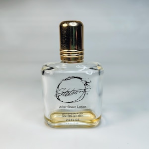 Pu&ograve; includere: Una bottiglia di vetro trasparente di lozione dopobarba Stetson con un tappo color oro. La bottiglia ha una forma quadrata con bordi arrotondati e un liquido color oro sul fondo. L'etichetta presenta il logo Stetson e il testo "After Shave Lotion".
