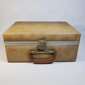 May include: A vintage tan suitcase with a brown handle and a metal clasp. The suitcase has a rectangular shape and a slightly worn appearance, suggesting it has been used. The handle is a curved, brown plastic. The metal clasp is a dull gold color.