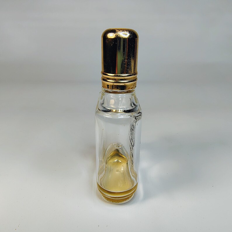 Pu&ograve; includere: Piccola bottiglia di profumo in vetro trasparente con tappo e dettagli dorati. La bottiglia ha una forma rettangolare con bordi arrotondati e contiene una piccola quantit&agrave; di liquido color ambra. Il tappo &egrave; cilindrico.