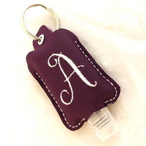 May include: A purple leather keychain with a white embroidered letter A and a clear hand sanitizer bottle attached.
