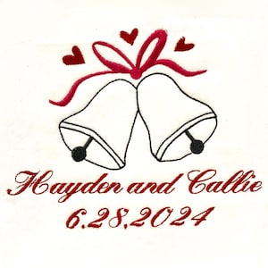 Puede incluir: Campanas de boda blancas bordadas con una cinta roja y corazones, con el texto "Hayden y Callie 6.28.2024" en rojo.