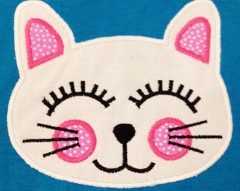 May include: White felt applique of a cat with pink ears, pink cheeks with white polka dots, black eyes, and a black nose. The cat is smiling with its eyes closed.