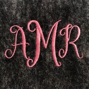 Peut inclure: Lettres brodées roses "AMR" sur un fond flou gris foncé.