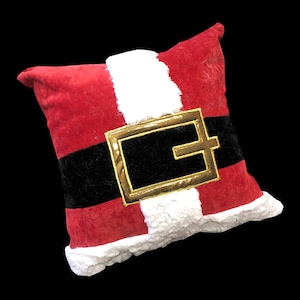 May include: Red and white plush pillow with a black belt and gold buckle, resembling Santa's belt.