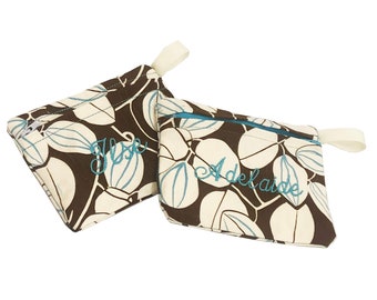 May include: Two fabric pouches with a floral pattern in brown, cream, and teal. One pouch is triangular, the other rectangular. Both have teal zippers and cream-colored loops. The triangular pouch has the name "Jose" embroidered in teal, and the rectangular pouch has "Adelaide".