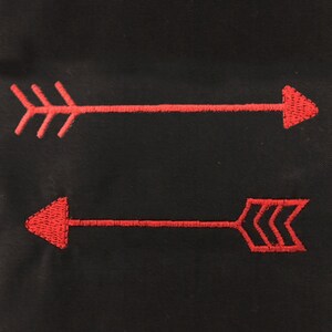 May include: Two red embroidered arrows pointing in opposite directions on a black fabric background.