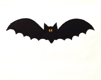 Puede incluir: Un murciélago negro de fieltro con alas extendidas y ojos amarillos. El murciélago tiene un borde de ala festoneado y está sobre un fondo blanco. Ideal para decoraciones de Halloween.
