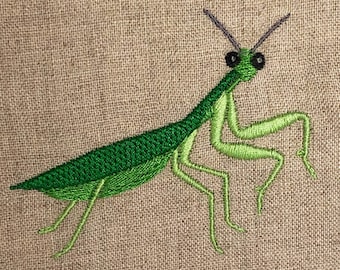 May include: Green embroidered praying mantis with long legs and large eyes on a beige fabric background.