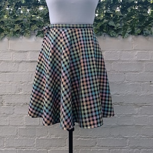 Puede incluir: Una camiseta sin mangas blanca combinada con una falda a cuadros colorida en tonos pastel de rosa, amarillo, azul y negro. Un collar de cadena dorada adorna el cuello del maniquí. La falda tiene un diseño acampanado.