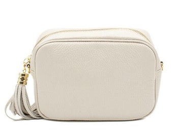 May include: A cream-colored leather crossbody bag with a gold zipper and a tassel.