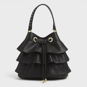 May include: A black bucket bag featuring three horizontal tiers of ruffled fabric layers. The bag includes a drawstring closure with gold-toned metal eyelets and a single top handle adorned with small, evenly spaced gold-toned metal studs.