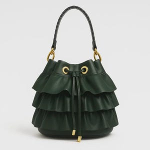 May include: A dark green bucket bag featuring three horizontal ruffled layers around the body. The bag includes a black braided top handle attached with gold-toned metal rings, and a drawstring closure with gold-toned eyelets and metal tips.