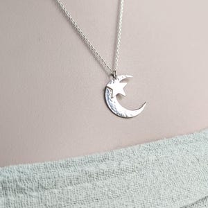 Op de afbeelding: Een zilveren ketting met een maan- en sterhanger. De hanger heeft een gehamerde textuur en hangt aan een fijne ketting. De ketting wordt getoond tegen een neutrale achtergrond.